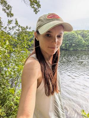 woman in hat poses in front water