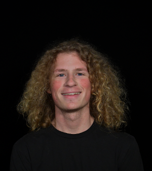 Man with blonde, long curly hair wearing black shirt with black background